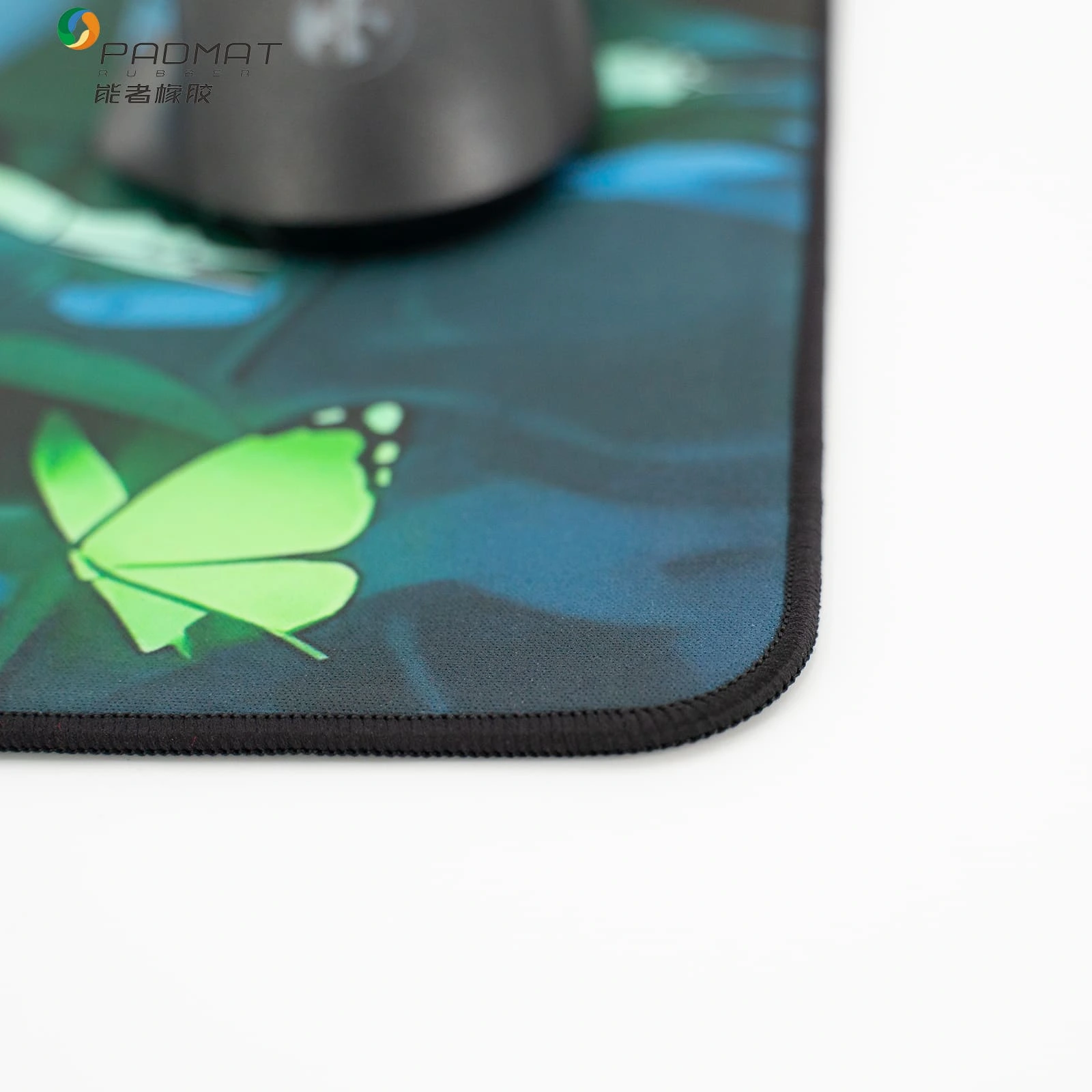 Close-up of Ghost Tracks mouse pad corner showing green butterfly design and durable lock stitching edge