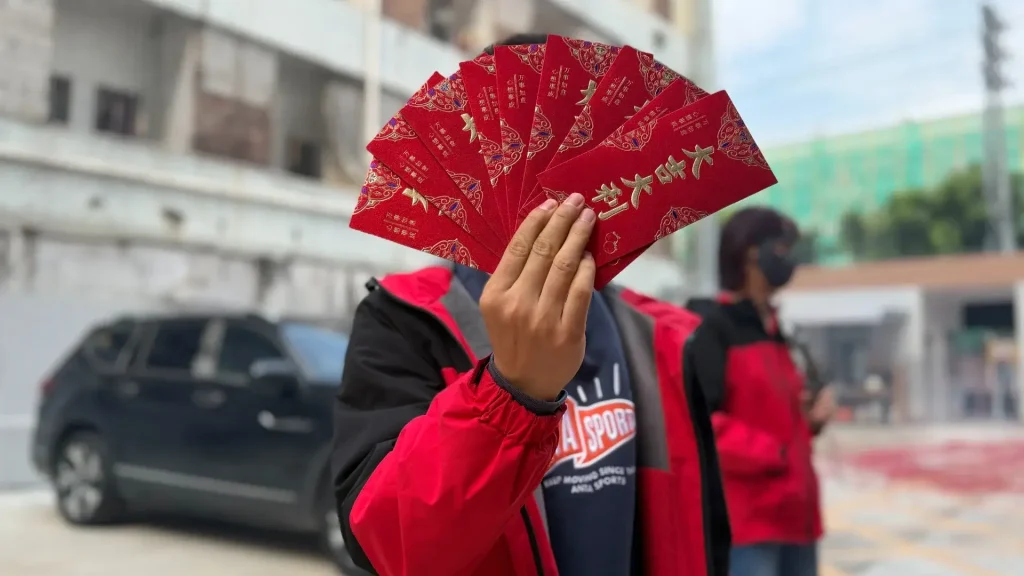 Hand holding fan of lucky red envelopes at Padmat Rubber factory for Chinese New Year celebration