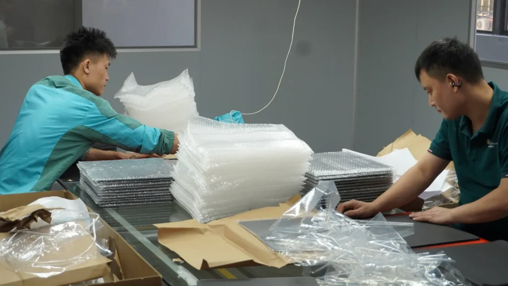 Workers packing custom mousepads with bubble wrap and cartons at Padmat Rubber factory