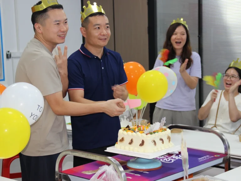 Close shot of birthday representatives cutting cake at office quarterly birthday party, colorful balloons, colleagues cheering beside