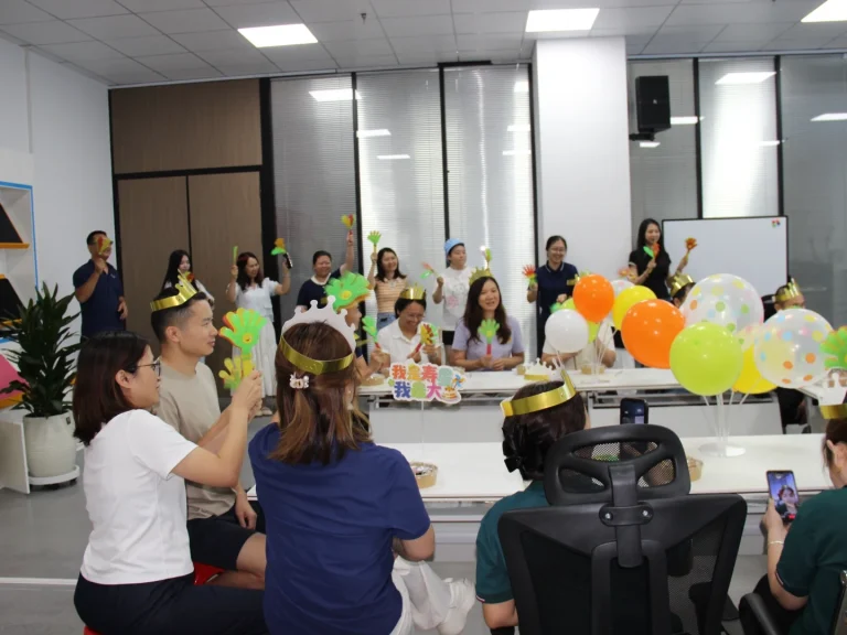 Office quarterly birthday party group photo, employees wearing golden birthday crowns, balloons and cheering clappers for collective birthday celebration