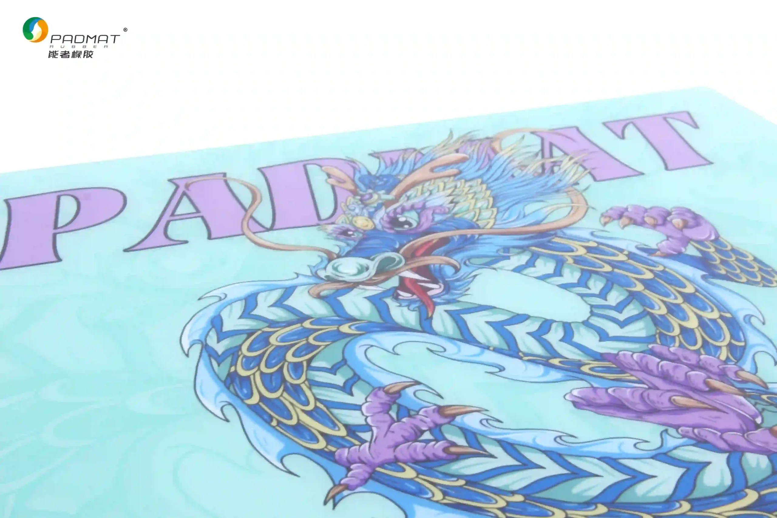 Tilted view of Padmat glass gaming mouse pad showing blue dragon artwork, purple brand logo, and fine glass surface texture with cyan background.