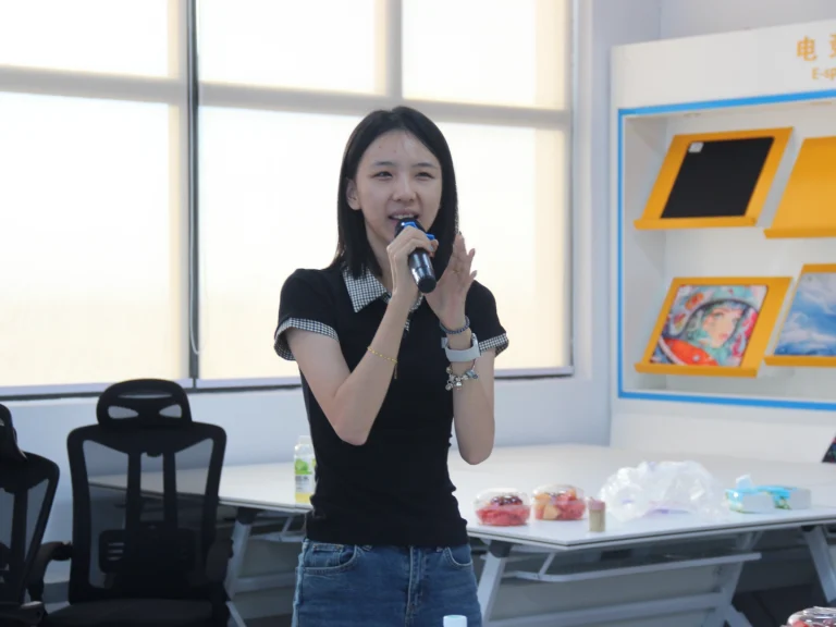 New female employee holding microphone to introduce herself during Padmat Rubber new staff welcome event, esports mouse pad display area in background