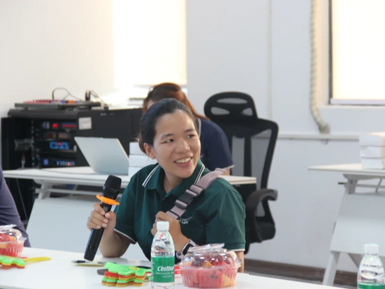 Staff holds microphone to share feelings after joining Padmat Rubber, fruit platters placed on desktop in relaxed communication atmosphere